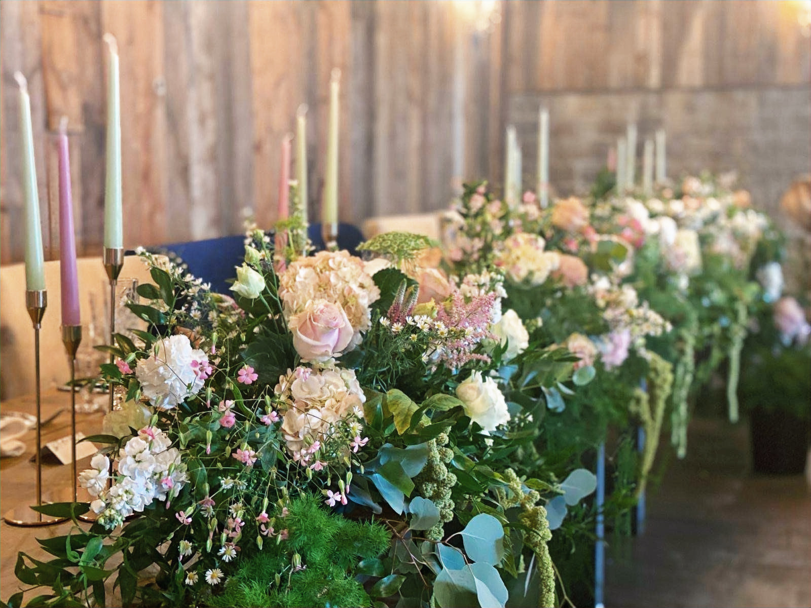 Reception table dressed with low urn arrangements of seasonal blooms